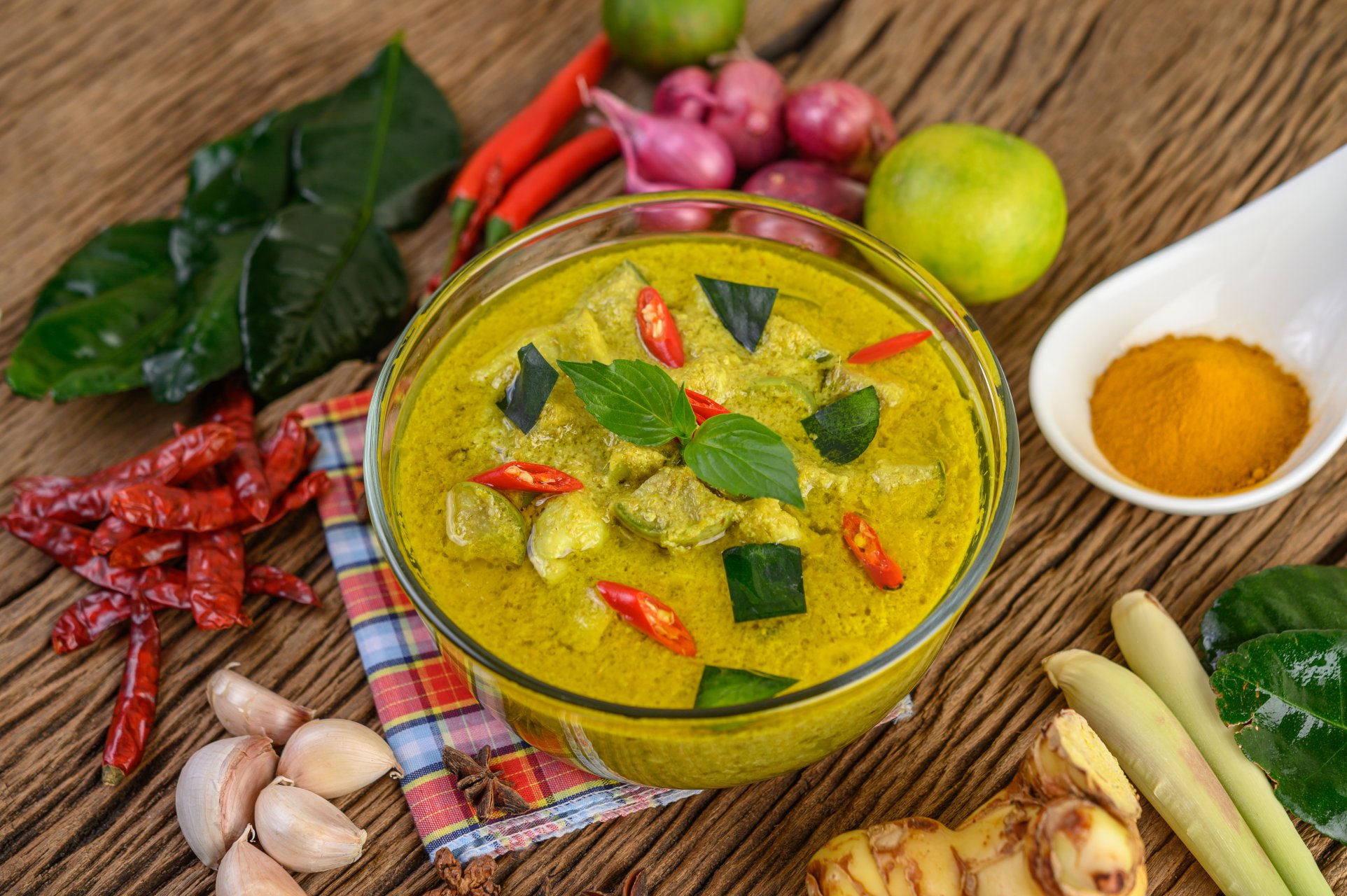 Green curry in a bowl and spices on wooden table.
