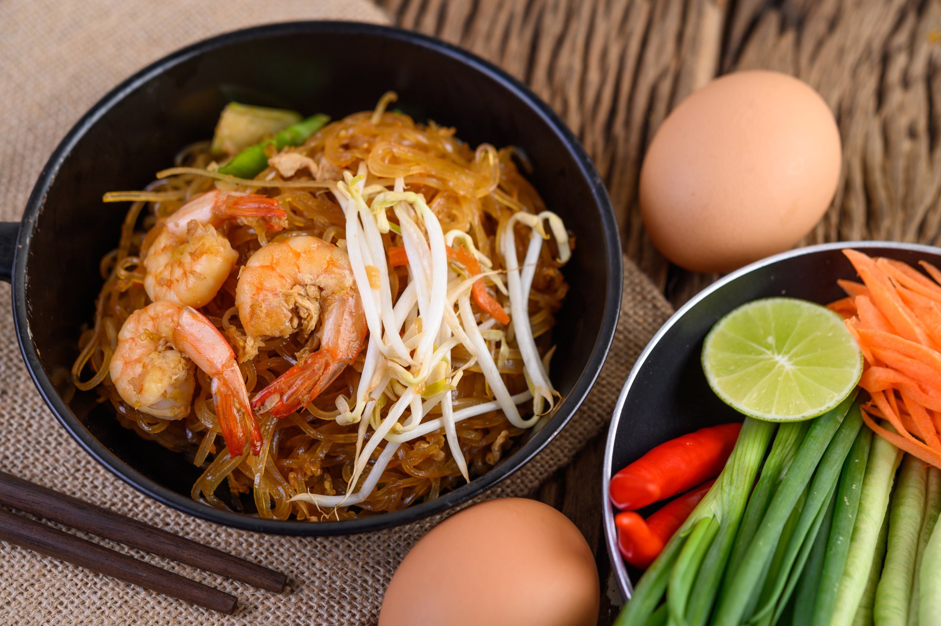 Padthai shrimp in a black bowl with eggs and Seasoning on wooden table.